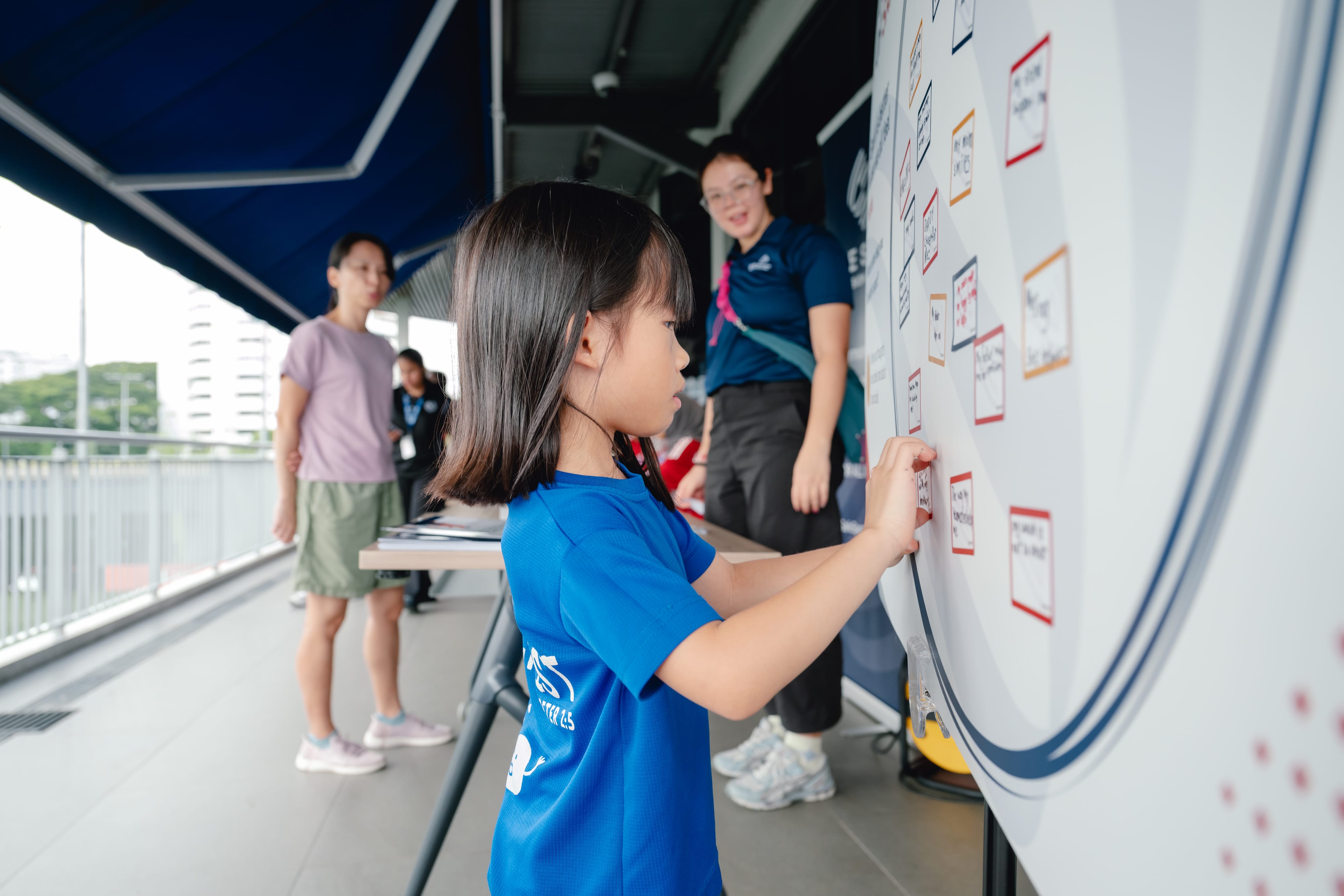 A girl wearing a blue shirt is engaged in sticking a sticker on a board, demonstrating concentration.